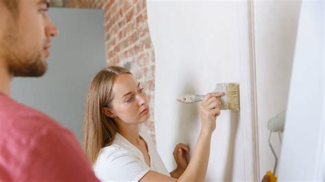 Detailní záběr na nanášení barvy válečkem na stěnu ve tvaru písmene 